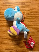 Side view of light blue Yoshi plush showing tag and shoes