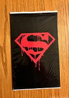 Front of sealed black polybag showing red dripping Superman logo