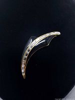 Full view of black enamel gold-tone curved brooch with rhinestone row