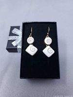 Front view of earrings in box showing white shell spirals and gold-tone metal