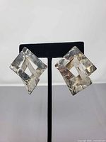 Front view of earrings on stand showing interlocking square design and hammered texture