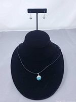 Full view of pendant necklace on bust with matching earrings on stand