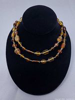 Full view of double-looped amber glass bead necklace on display bust
