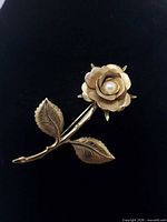 Front view of gold tone rose brooch with faux pearl centre