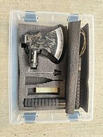 Complete multitool axe kit in open case showing axe head, handle sections, spike, stone and foam insert