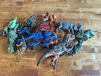 Group shot of all plastic dinosaur, dragon and wolf figurines on wooden surface