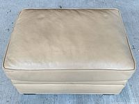 Top view of beige leather ottoman showing cushion surface and piping