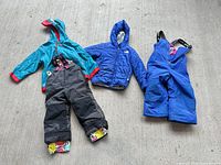 All four pieces laid flat: teal jacket, grey-black pants, blue The North Face jacket, blue bib snow pants