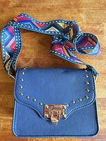 Front view of blue leather studded handbag with multicolor strap