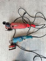 Two corded angle grinders with cords, side handles and grinding wheels