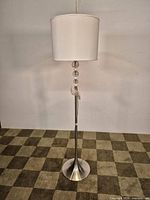 Full view of chrome floor lamp showing shade, stem with glass spheres, flared base
