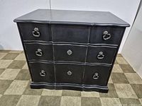 Front three-quarter view of black serpentine-front chest showing drawers and hardware
