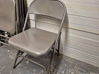 Stack of gray metal folding chairs showing seat, backrest and tubular frame