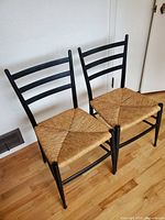Front angled view of the two black ladder-back chairs showing frames and woven seats