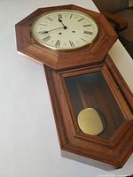 Front view showing full clock, octagonal face, lower glass door with brass pendulum