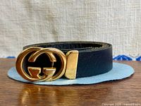 Front view of belt showing gold interlocking GG buckle and black leather strap