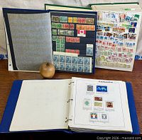 Front view of three binders/stock books showing mounted Canadian stamps, apple for scale