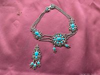 Necklace arranged in U shape with detached drop piece on pink surface