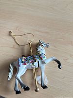 Full view of white resin carousel horse ornament with gold pole and hanging string