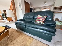 Front angled view of the forest green leather loveseat showing overall style and condition