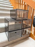Five plastic shoe bins stacked on staircase, showing clear doors