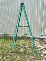 Full view of folded green fiberglass A-frame ladder outdoors