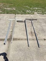 Three steel poles with brace plates laid out on pavement