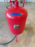 Full view of red Central Pneumatic blast pot on wheels with hose attached