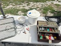 Overall lot on table showing tackle box, bucket, styrofoam light, battery leads, mesh platform, net