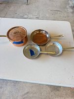 Saucepan with lid and two frying pans on table