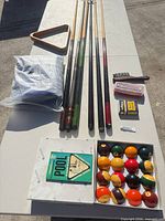 Lot overview showing cues, balls, rack, brush, chalk, manual