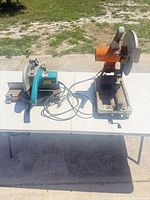 Two stationary metal chop saws on table, showing overall condition, bases, blades, and cords