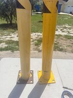 Two yellow steel bollards standing side by side on table, showing overall condition and flange bases