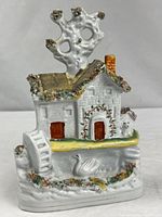 Front view of ceramic cottage figurine showing bocage tree, windows, doors, swan and base