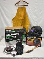Entire lot displayed: welder box, helmet box, apron, gloves, wire spool, grinder wheels, brush