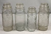 Front view of all four clear glass Mr. Peanut canister jars showing differing patterns and lids