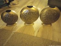 Front view of three embossed silvery bronze iron vases, showing graduated sizes and floral design