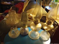 Four glass oil lamps with chimneys and shades on blue surface