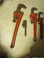 All four pipe wrenches arranged side by side on floor showing relative sizes and condition