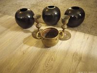 Three black ceramic vases, two brass candlesticks and a small brass pot displayed together