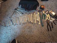 Overview of wrenches, pliers, hammers, tape measure and tool bag spread on floor