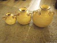Front view of three graduated beige stoneware jugs showing size differences, dual side handles and rustic brown accenting