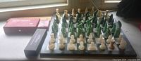 Chess board with full set of green and cream stone pieces, red domino box, black novelty domino box
