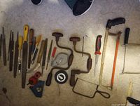 Group of vintage hand tools laid out on floor: bit braces, files, saws, screwdrivers, tape reel