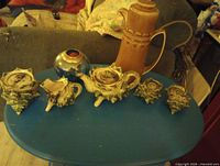 All seven items on blue table: tall brown pitcher, five beige shell-shaped ceramic pieces, blue glass vase