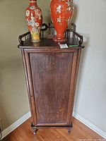 Front view of tall narrow wood cabinet showing carved door and top rail