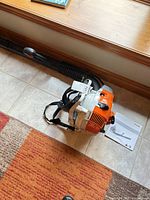 Leaf blower laid on floor with blower tube attached and manual beside it