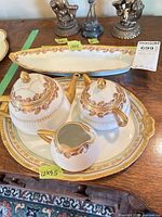 Set displayed on wooden table: teapot, sugar, creamer on round underplate; long tray behind