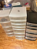 Three tall plastic drawer towers side by side with small organizers on table behind