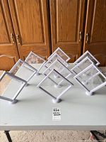 Eight white plastic square display frames on bases shown